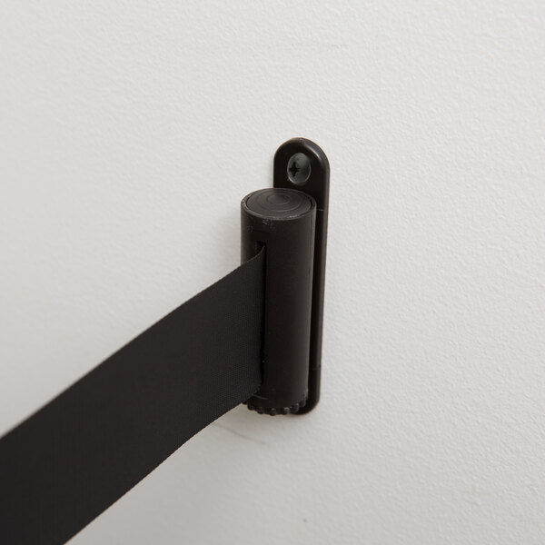 A black metal bracket on a white wall with a black tape attached.