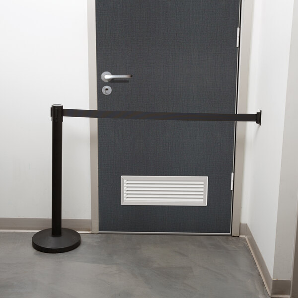 A black Aarco wall mounted stanchion barrier on a door.