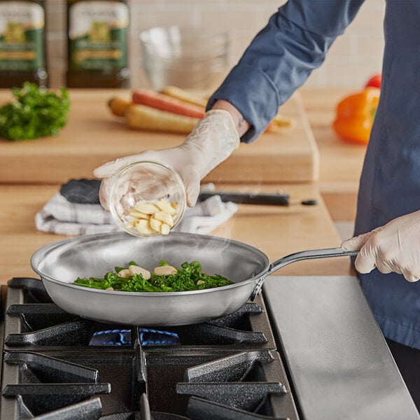 A person cooking food in a Vollrath stainless steel fry pan on a stove.