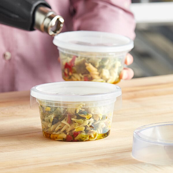 A person pouring food into a clear plastic container.