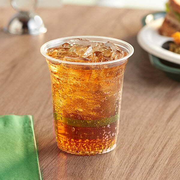 A World Centric plastic cup filled with a drink on a table with a sandwich.