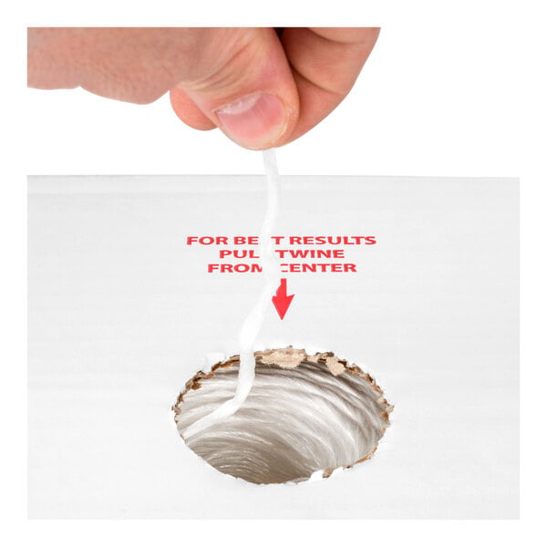 A hand is pulling a white twine from the center of a spool through a hole in a white box, with red text instructing to pull the twine from the center.