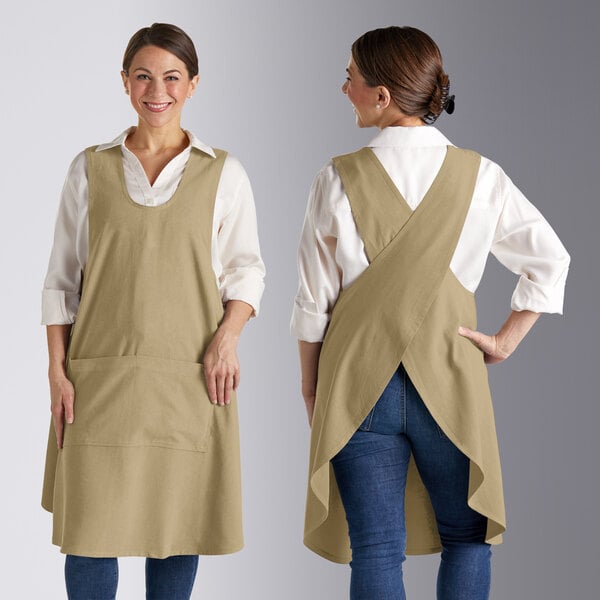 A woman wearing a sage green Acopa smock bib apron with pockets.