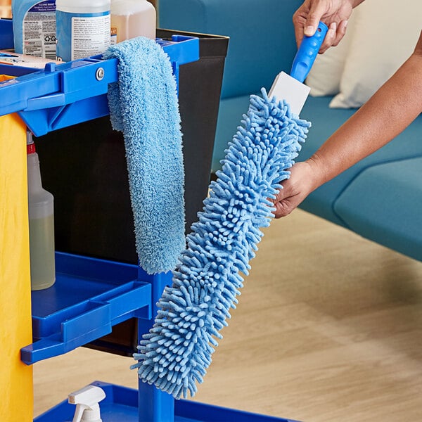 A hand holding a blue Lavex Flex Wand Duster with a blue microfiber sleeve and a blue chenille sleeve.