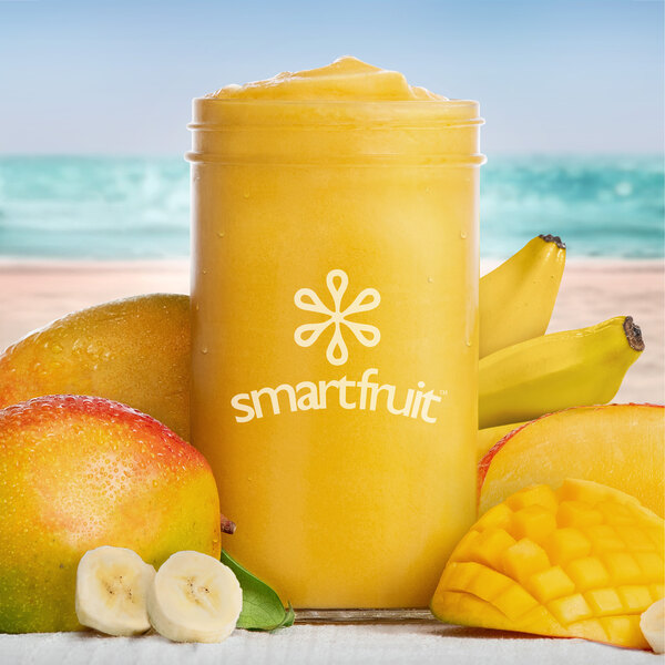 A jar of yellow Smartfruit Mellow Mango smoothie next to a banana and mango.