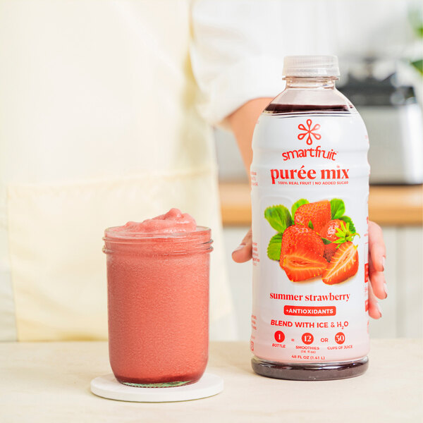 A woman's hand pours Smartfruit Summer Strawberry puree into a glass of pink liquid.