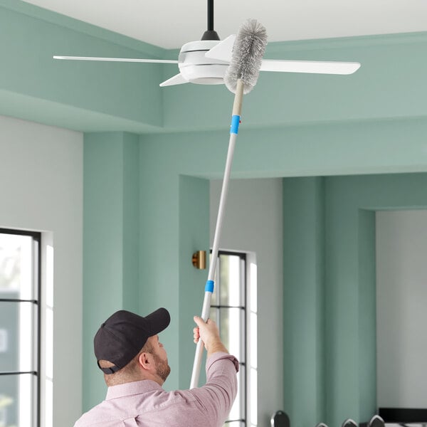 A man using a Lavex 15" Duster Brush to clean a ceiling fan.