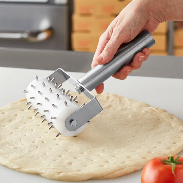 A hand with a stainless steel dough docker rolling dough.