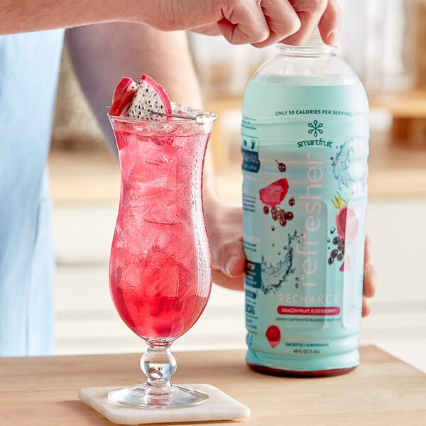 A person pouring Smartfruit Recharge Dragon Fruit and Elderberry refresher into a glass.