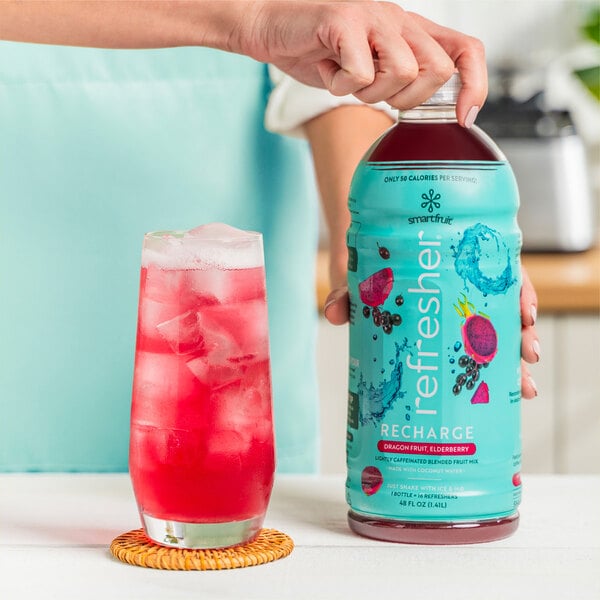 A person holding a Smartfruit Recharge Dragon Fruit and Elderberry refresher bottle.