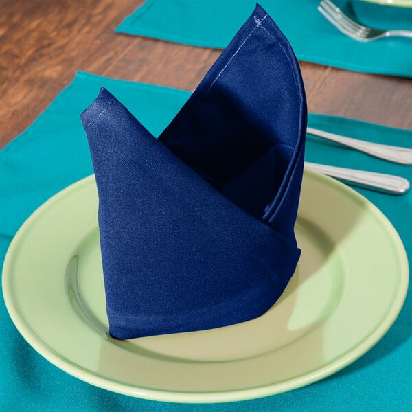 A folded royal blue polycotton blend Intedge cloth napkin on a plate.