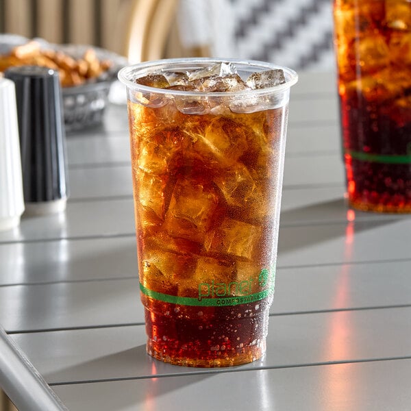 A clear 24 oz. compostable plastic cold cup filled with iced soda.