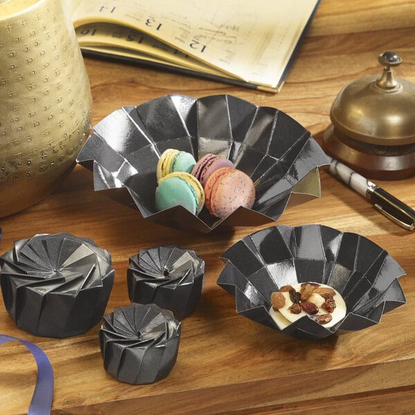 A group of Solia black cardboard origami bowls with food in them.