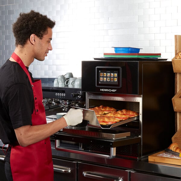 A Merrychef conneX16 high-speed oven in carbon black finish being used to bake croissants.