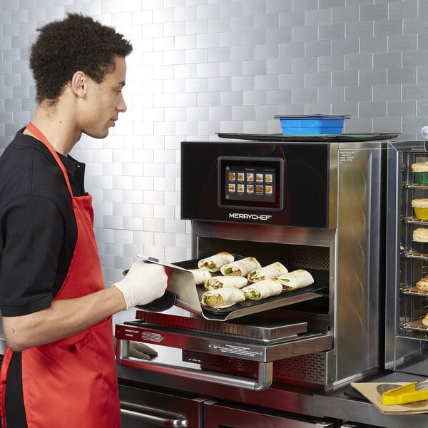 A man in an apron and gloves using a Merrychef conneX16 rapid cook oven to prepare food.