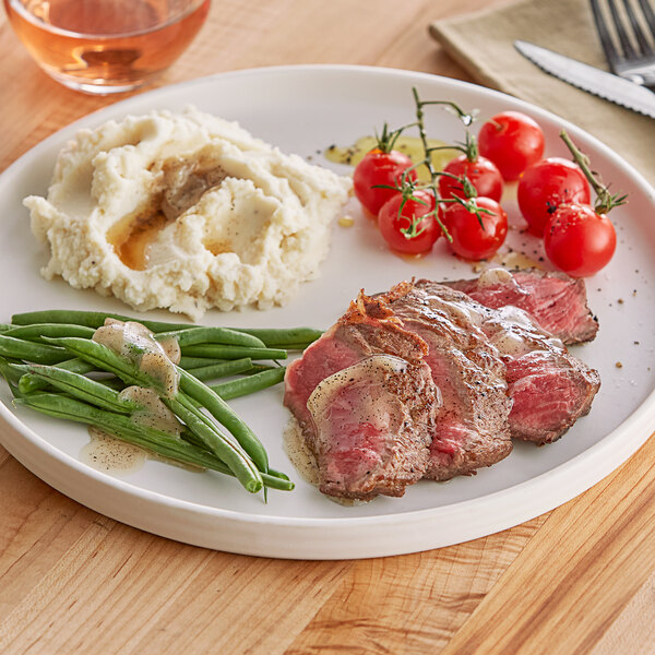 A plate with steak, mashed potatoes, and green beans served with Black & Bolyard Truffle Brown Butter on a table.