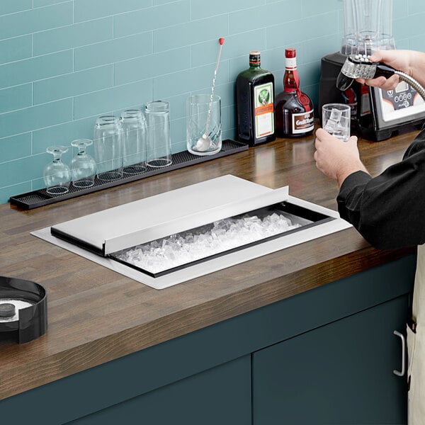 A man pouring a drink into a glass from a Regency stainless steel ice bin on a counter.