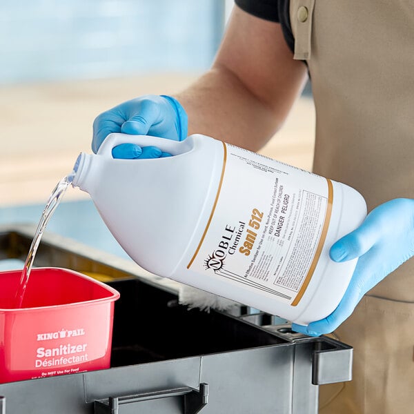 A person in blue gloves pouring Noble Chemical Sani-512 into a container.