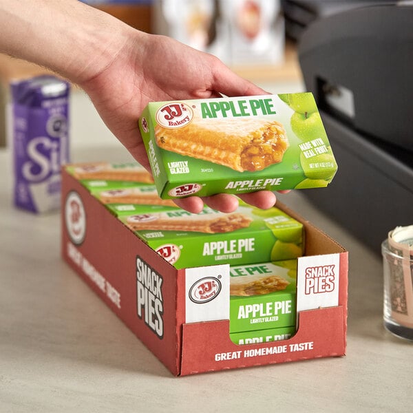 A hand holding a box of JJ's Bakery Apple Pie Turnovers.