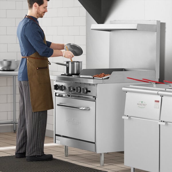 A man in a brown apron cooking on a Main Street Equipment natural gas range with griddle and oven.