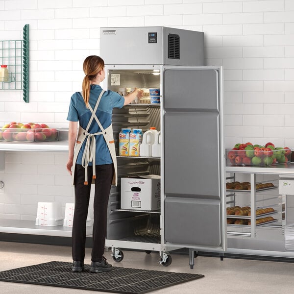 A woman wearing a white apron opening a Delfield reach-in refrigerator.