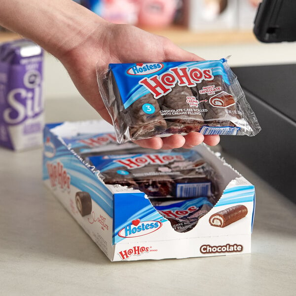 A hand holding a package of Hostess chocolate cake rolls with a blue label.