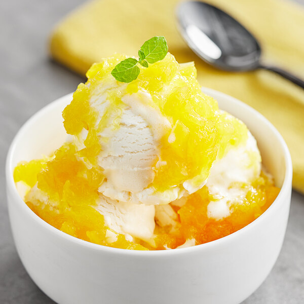 A bowl of ice cream topped with pineapple dessert, served with orange slices and mint.