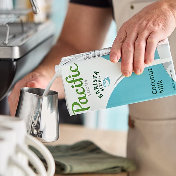 A carton of Pacific Foods Barista Series Coconut Milk being poured into a metal frothing pitcher.