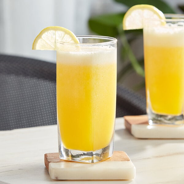 A glass of yellow Capora Lemonade with a lemon wedge on top.