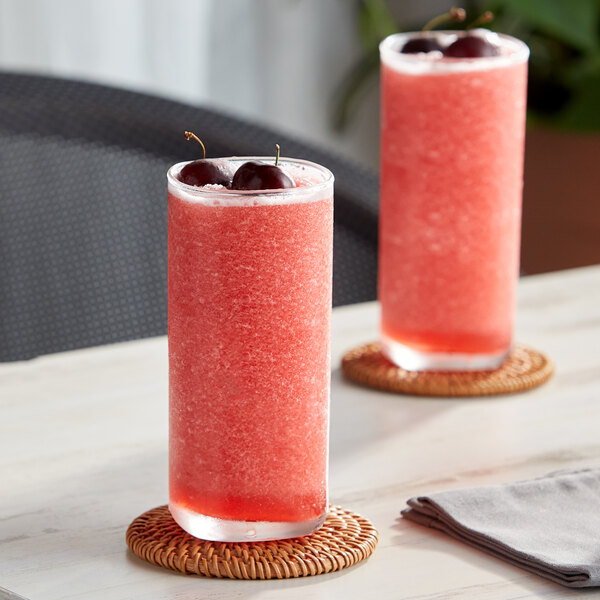 Two glasses of Capora cherry fruit smoothie with cherries on top.