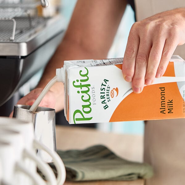 A carton of Pacific Foods Barista Series Almond Milk being poured into a metal pitcher.