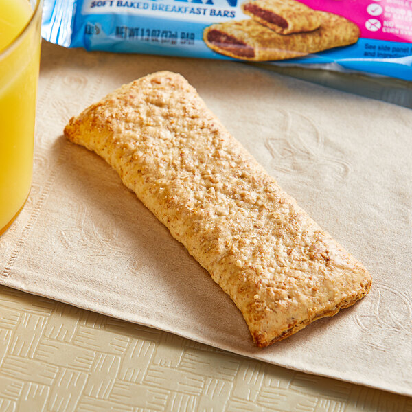 A Nutri-Grain Raspberry Cereal bar on a napkin next to a glass of yellow liquid.