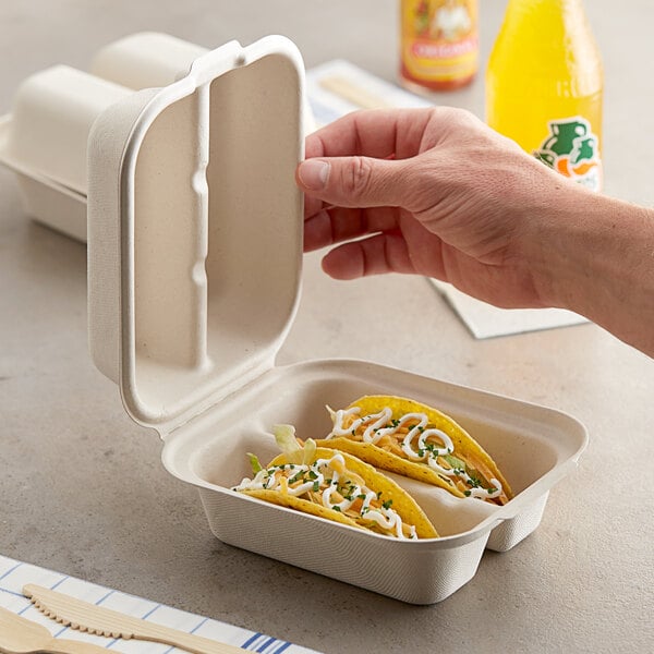 A hand opening a World Centric compostable fiber taco container with tacos inside.