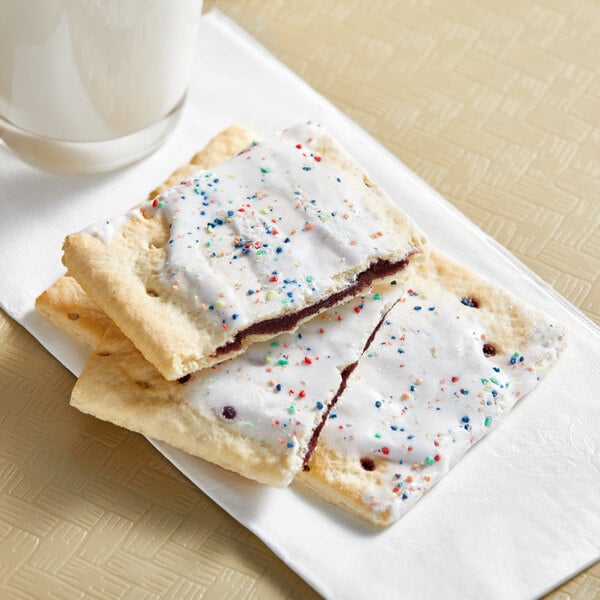 A white frosted Pop-Tart with sprinkles on a napkin with a glass of milk.