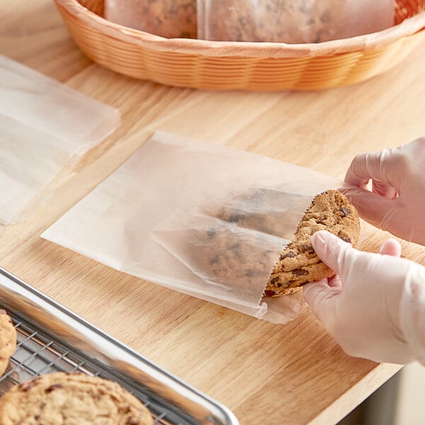 A person in gloves holding a cookie in a white waxed paper bag.