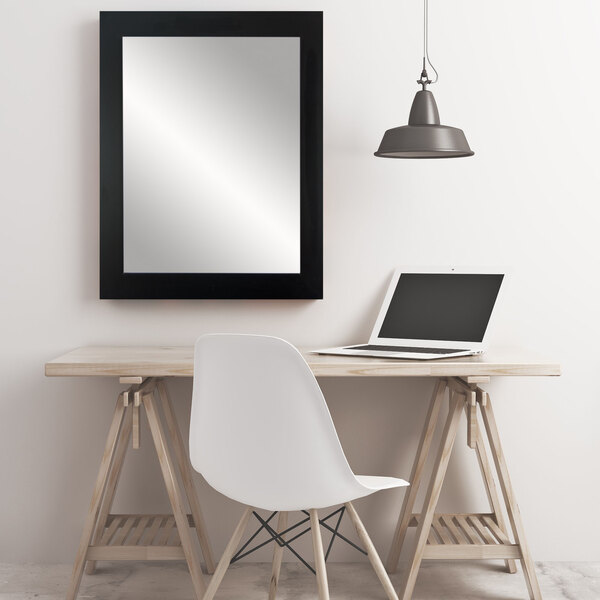 A BrandtWorks matte black rectangular mirror above a table with a white chair with wooden legs and a laptop.