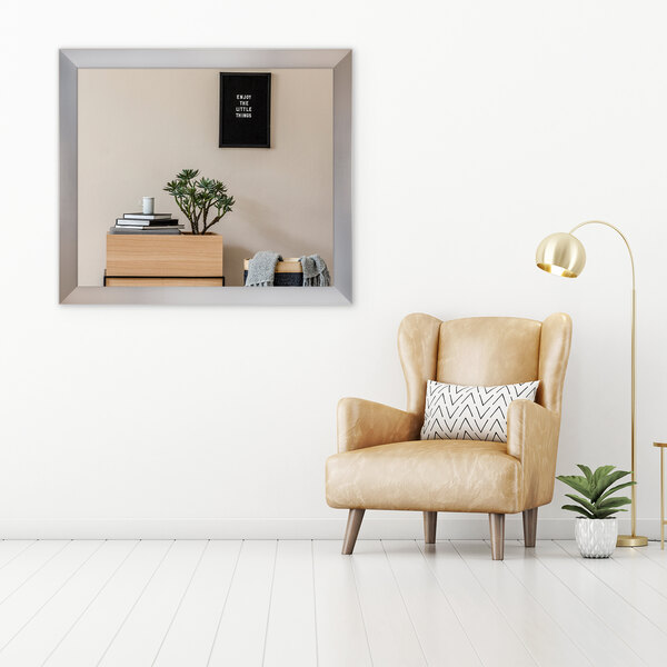 A BrandtWorks stainless steel mirror above a tan leather chair in a room.