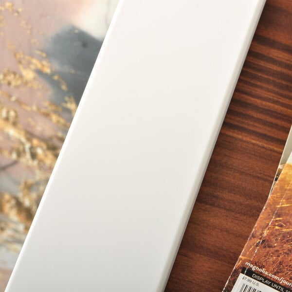 A BrandtWorks matte white rectangular mirror on a wood surface.