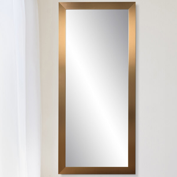A BrandtWorks champagne finish mirror with gold trim on a white wall.