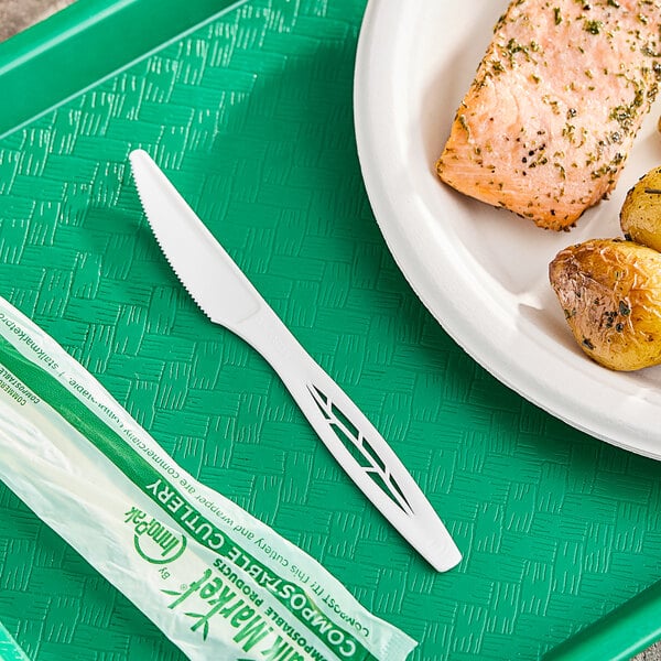 A white Stalk Market CPLA knife on a green surface next to a plate of salmon.