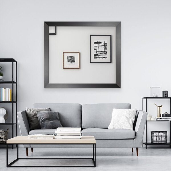 A BrandtWorks matte black mirror hanging on the wall in a living room with a gray couch and a coffee table.