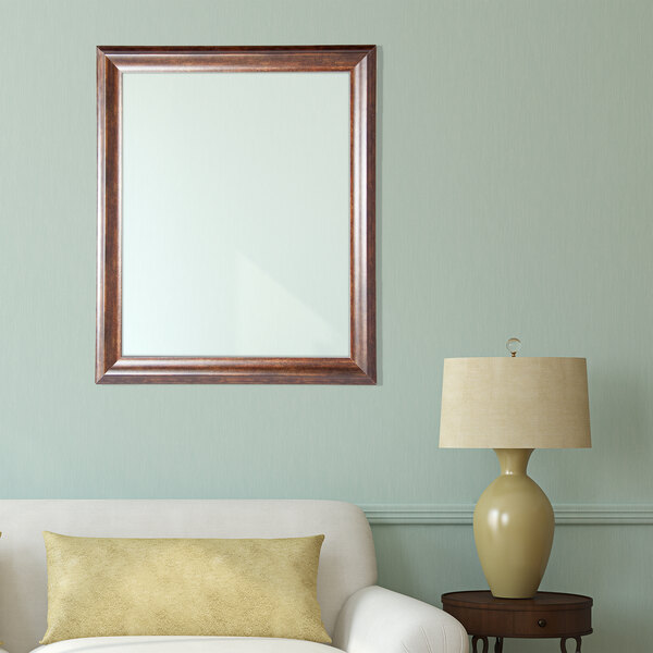A BrandtWorks copper brown mirror on a wall above a white couch with a brown cushion.