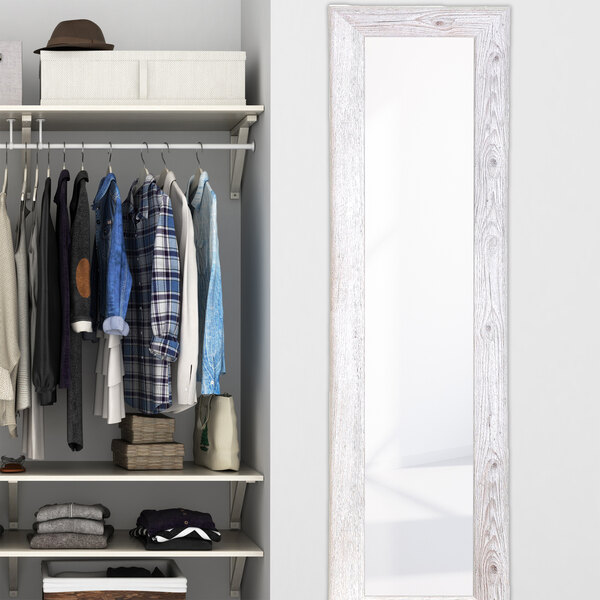 A BrandtWorks white farmhouse mirror hanging on a white wall with clothes on it.