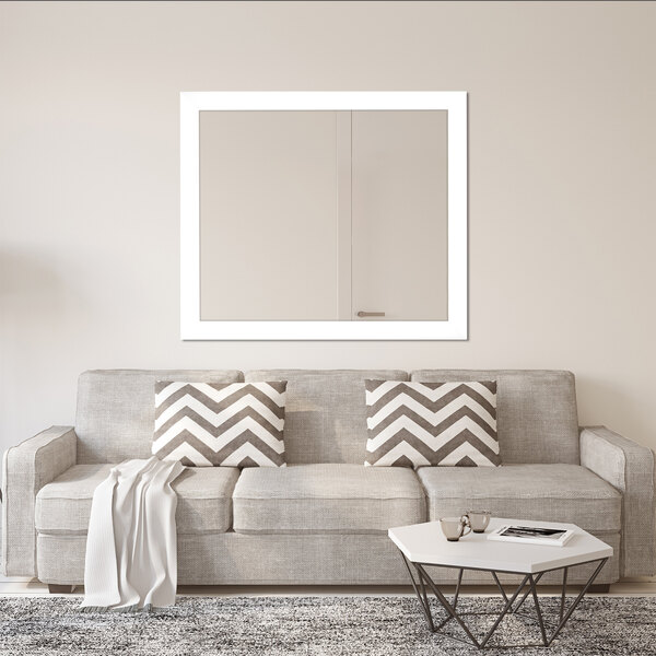 A BrandtWorks white wall mounted mirror above a couch with pillows.