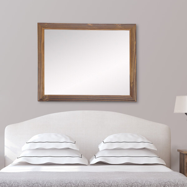 A BrandtWorks natural wood tone mirror mounted on the wall above a bed.