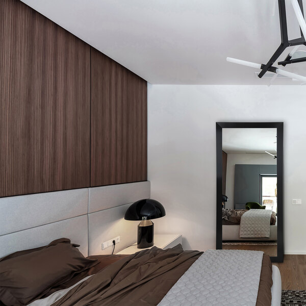 A BrandtWorks satin black mirror above a bed in a white bedroom with wood paneling.