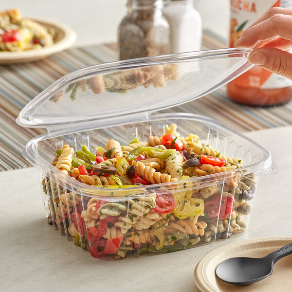 A person using a black spoon to take pasta from a Stalk Market clear plastic deli container.