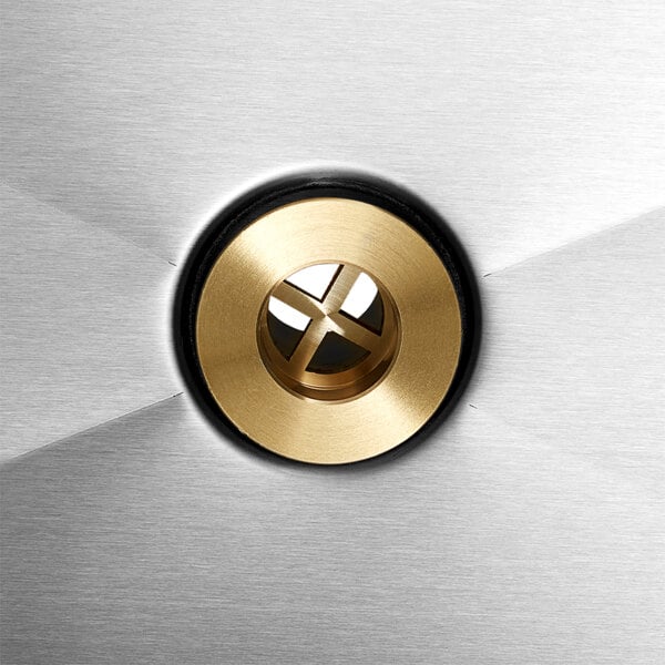 A close up of a circular brass button on a stainless steel surface.