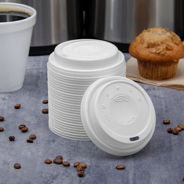 A white Dart travel lid on a stack of white plastic cups.