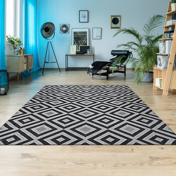 A Couristan Afuera Dipole runner rug with a black and white geometric pattern on a floor in a room with a chair and a shelf.